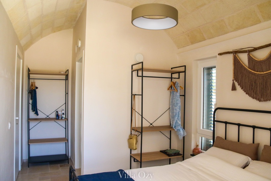 Second bedroom with iron-framed bed and woven wall hanging