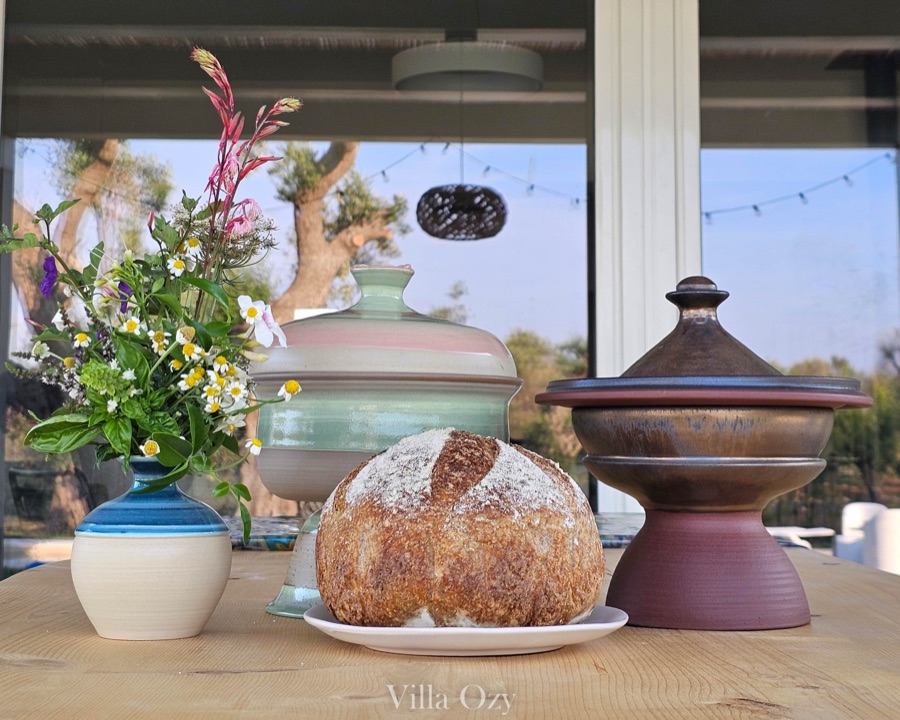 Kitchen still life: round country bread, ceramic vessels and a vase of wildflowers