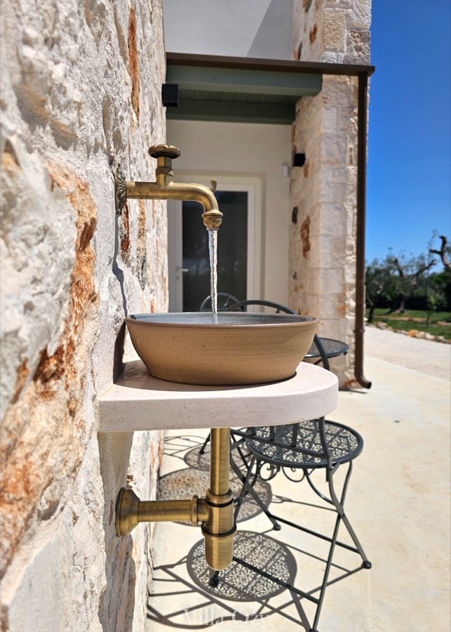 Brass tap above a ceramic basin set into a limestone wall